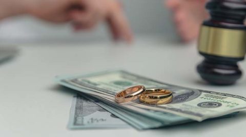Wedding rings on a stack of cash next to a gavel