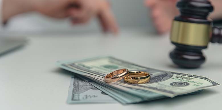 Wedding rings on a stack of cash next to a gavel